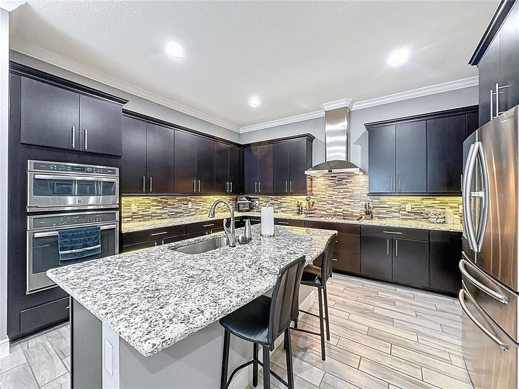107 Balmy Coast Road Groveland, FL 34736 - Photo 22 of 97 a kitchen with stainless steel appliances kitchen island granite countertop a table chairs in it and wooden floors