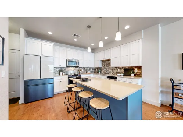 a kitchen with stainless steel appliances kitchen island granite countertop a refrigerator a stove a sink a dining table and chairs with wooden floor