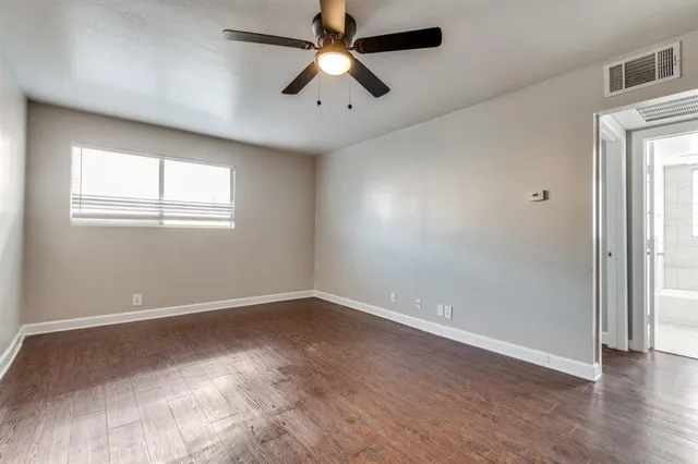 an empty room with wooden floor chandelier fan and windows