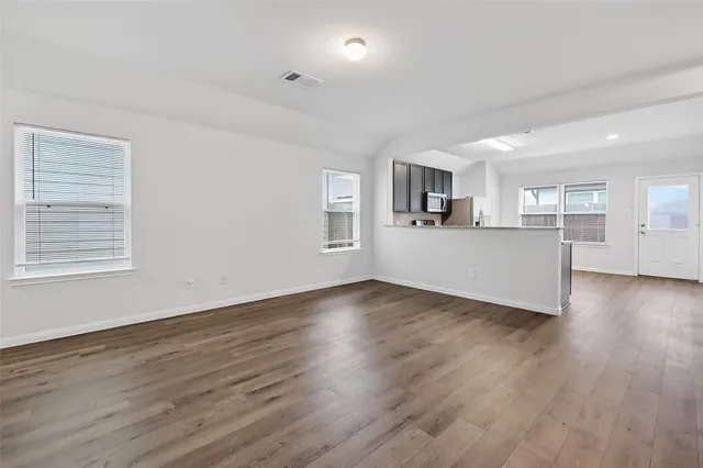 a view of a kitchen and an empty room with wooden floor and windows