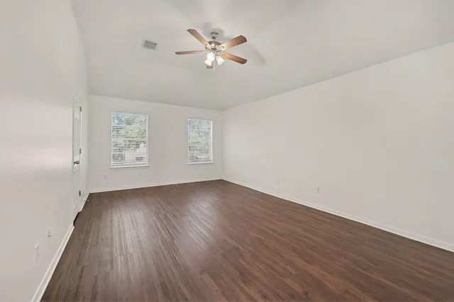 an empty room with wooden floor chandelier fan and windows