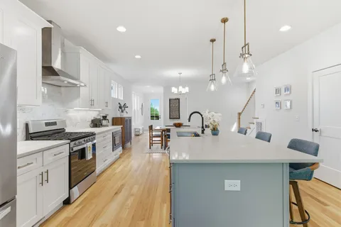 a large kitchen with stainless steel appliances a large counter top a stove a sink dishwasher and a refrigerator with wooden floor
