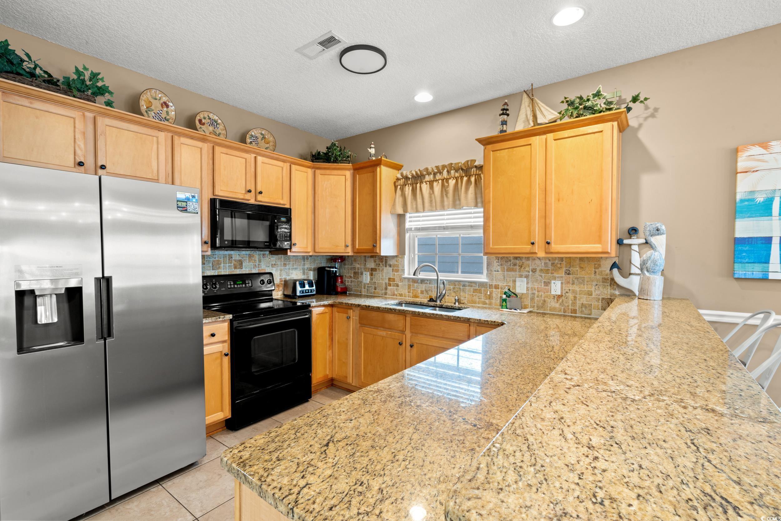 113 B 15th Avenue South Surfside Beach, SC 29575 - Photo 6 of 40 Kitchen featuring black appliances, a textured ceiling, tasteful backsplash, light brown cabinetry, and light stone counters