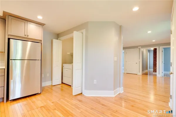 a view of an empty room with wooden floor and a kitchen