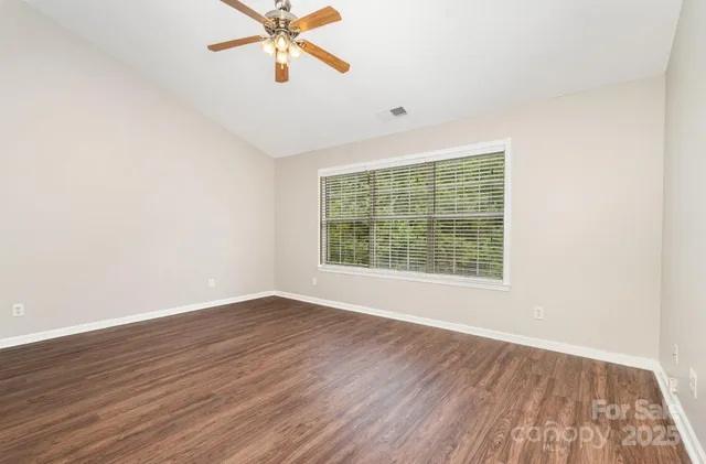 an empty room with wooden floor fan and windows
