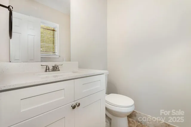 a bathroom with a granite countertop toilet a sink a mirror and a window