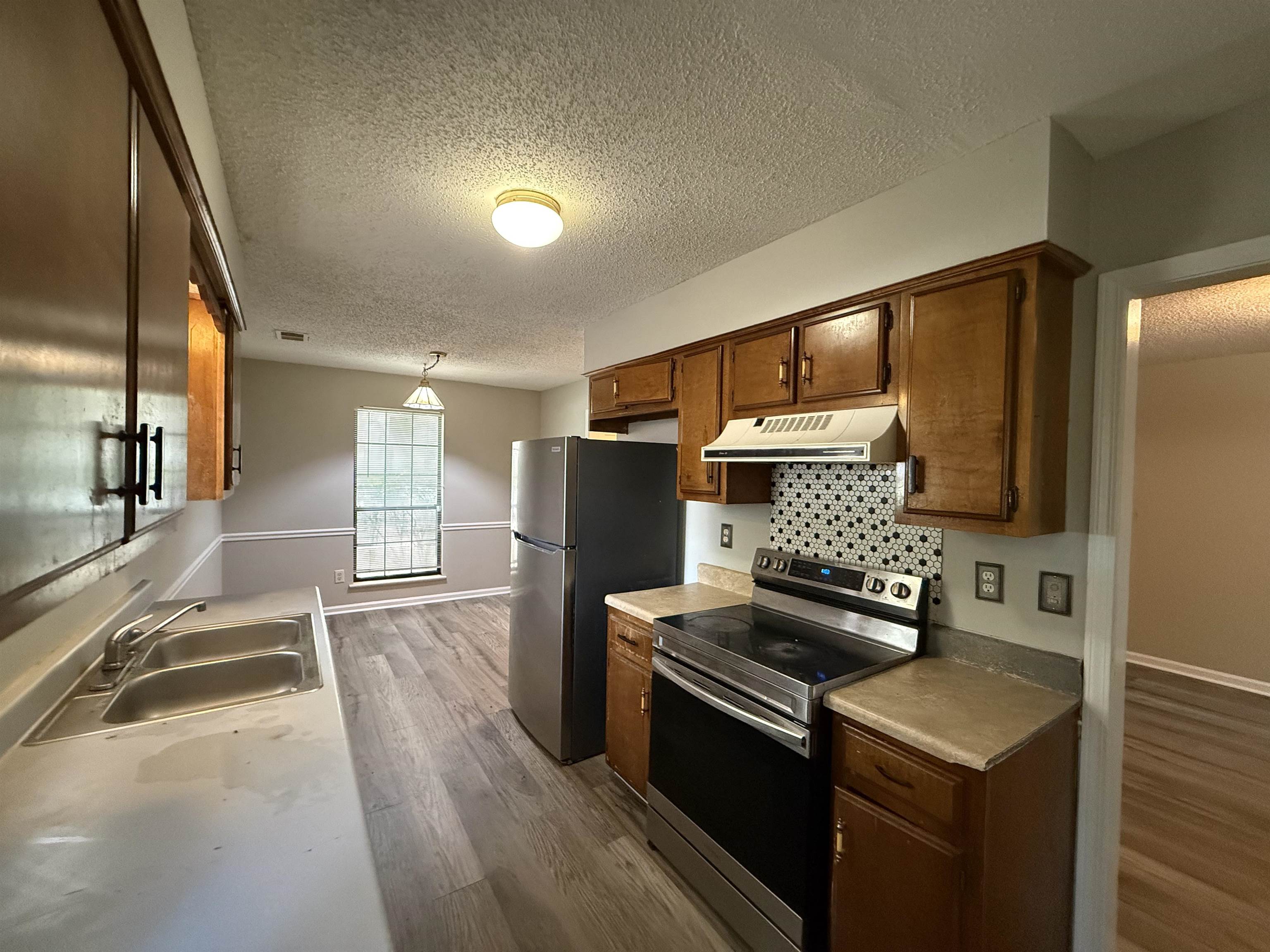 6420 Saginaw Road Memphis, TN 38134 - Photo 5 of 38 Kitchen featuring wood cabinetry, stainless steel appliances, a black and white geometric tile backsplash, and light wood-finish flooring
