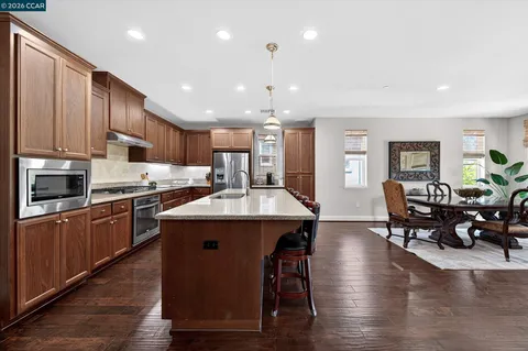 a kitchen with stainless steel appliances kitchen island granite countertop a table chairs and a refrigerator