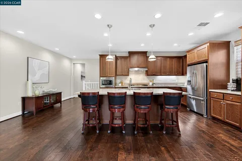 a kitchen with stainless steel appliances kitchen island granite countertop wooden floors refrigerator and dining table