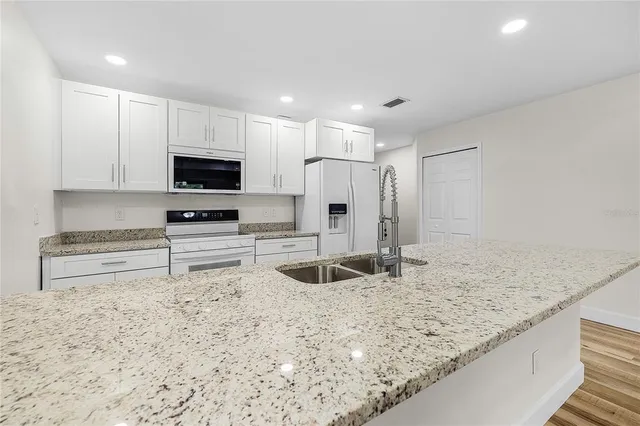 a large white kitchen with granite countertop a sink and dishwasher a stove top oven with wooden floor