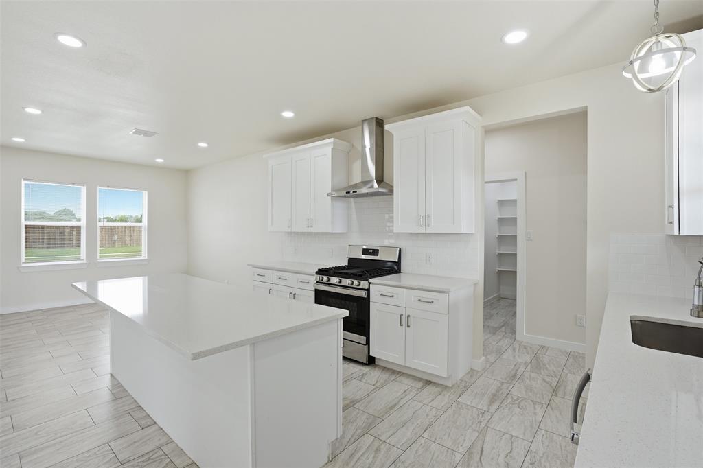 532 Highview Court Godley, TX 76044 - Photo 25 of 39 Contemporary kitchen featuring a large central island with a solid surface countertop, white cabinetry, stainless steel range with overhead hood, and light-toned tile flooring
