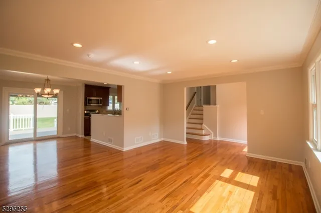 a view of an empty room with wooden floor and a kitchen
