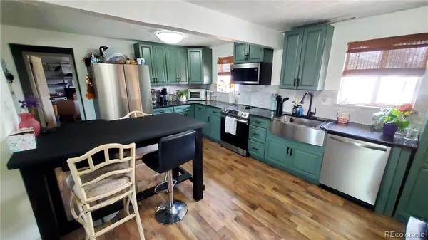 a kitchen with stainless steel appliances granite countertop a refrigerator a sink dishwasher a stove a dining table and chairs with wooden floor