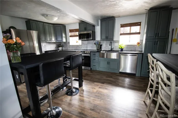 a kitchen with stainless steel appliances a stove a sink a microwave a refrigerator a stove a microwave and wooden floors