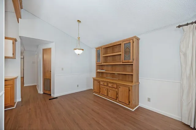 a view of an empty room and kitchen with wooden floor
