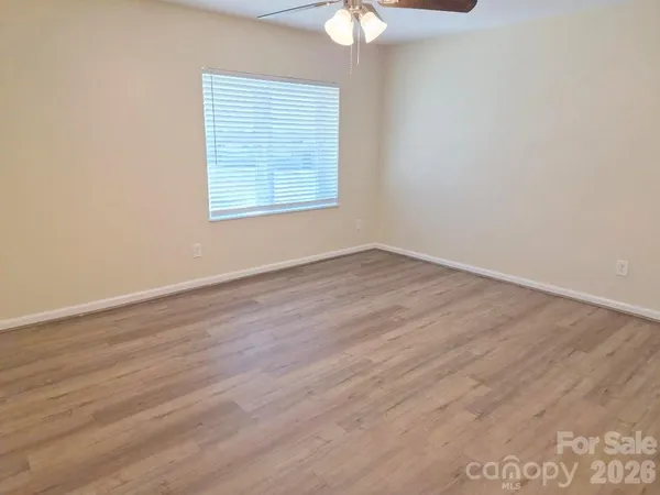 an empty room with wooden floor chandelier fan and windows