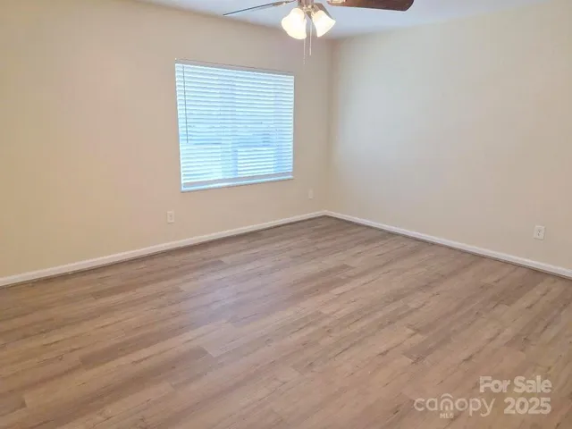 an empty room with wooden floor chandelier fan and windows