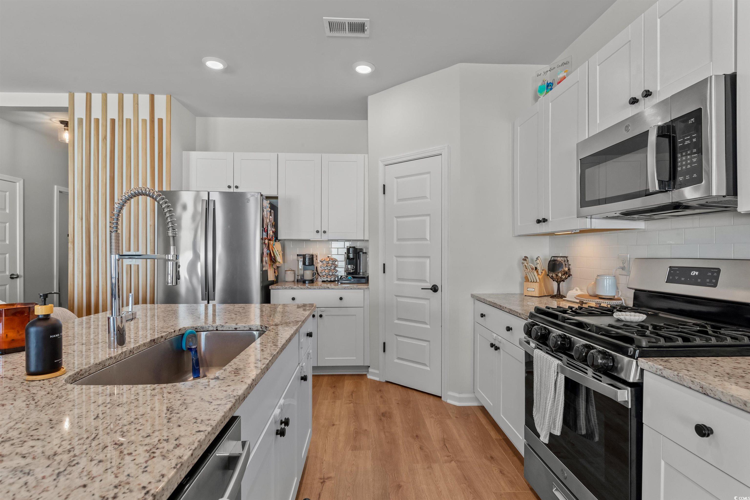 1067 Saltgrass Way Myrtle Beach, SC 29588 - Photo 22 of 40 Kitchen featuring appliances with stainless steel finishes, light wood finished floors, white cabinets, recessed lighting, and light stone counters