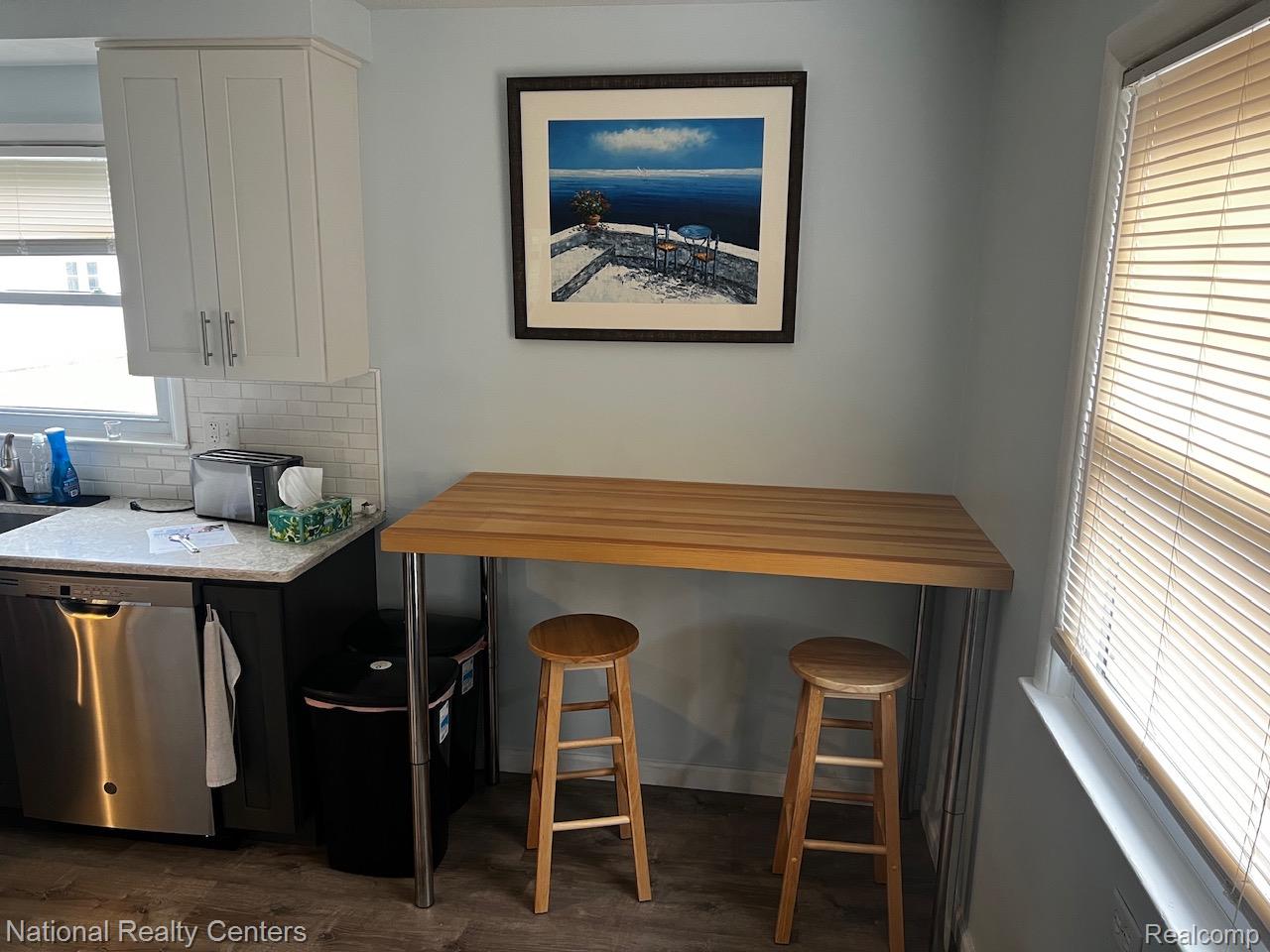 White shaker-style upper cabinetry, granite-style countertops, stainless steel dishwasher, white subway tile backsplash, and light wood-finish flooring