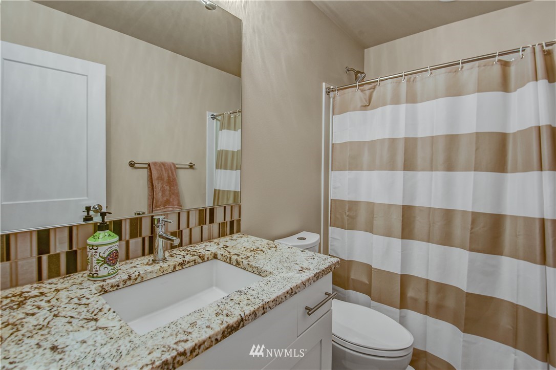 22810 23rd Avenue Southeast, Unit 2 Bothell, WA 98021 - Photo 13 of 16 a bathroom with a granite countertop sink a toilet a mirror and shower curtain