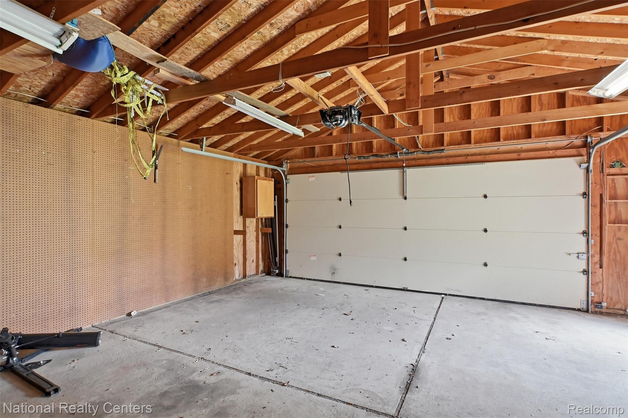 17159 Rougeway Street Livonia, MI 48152 - Photo 32 of 36 Garage featuring exposed wood beam ceiling, concrete flooring, pegboard wall, and an overhead garage door with opener