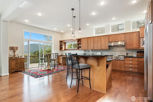 a open kitchen with granite countertop a stove top oven a sink a dining table and chairs with wooden floor