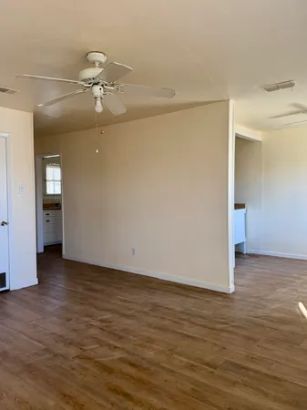 a view of an empty room with wooden floor and a ceiling fan