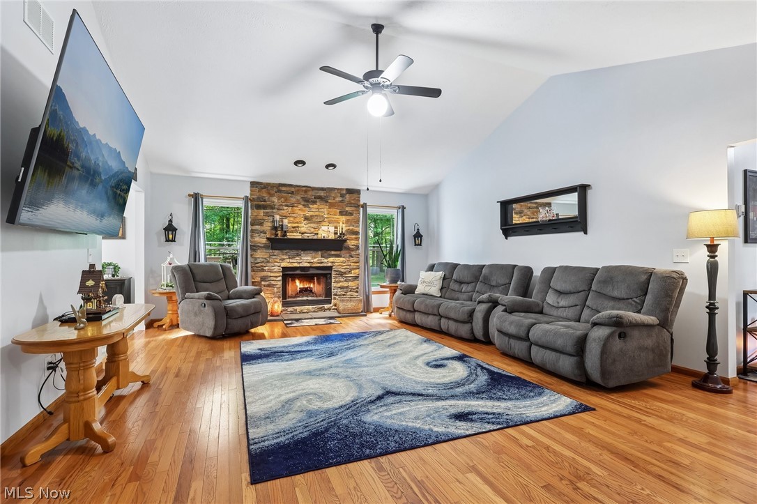 3213 Bates Road Madison, OH 44057 - Photo 5 of 45 Living area featuring a floor-to-ceiling stone fireplace with a wood mantle, vaulted ceilings, wood-finish flooring, and a ceiling fan with integrated lighting