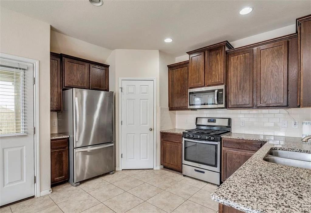 104 Beech Creek Lane Leander, TX 78641 - Photo 3 of 13 Kitchen with appliances with stainless steel finishes, dark brown cabinets, light stone counters, backsplash, and recessed lighting