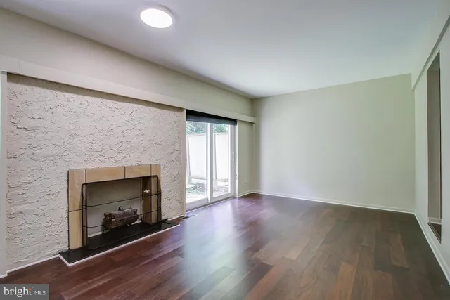 an empty room with wooden floor fireplace and windows