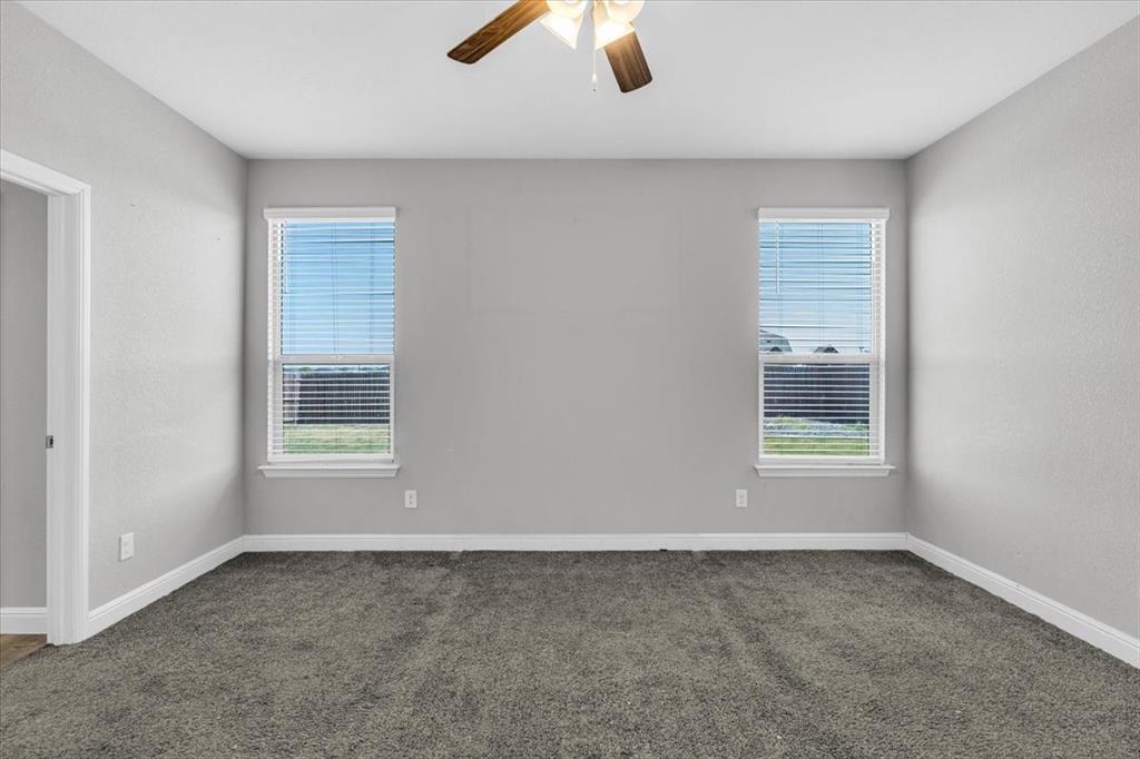 1402 Pleasanton Road Cleburne, TX 76033 - Photo 17 of 36 Neutral wall finishes, two windows with blinds, ceiling fan with light fixture, and dark gray carpeting
