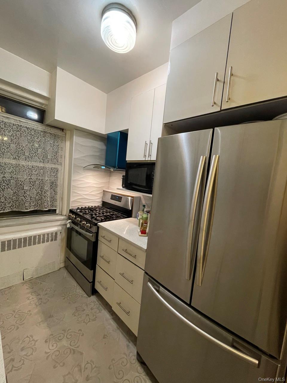 63-60 102nd Street, Unit D7 Queens, NY 11374 - Photo 38 of 41 Kitchen featuring appliances with stainless steel finishes, radiator, light tile patterned flooring, light stone counters, and backsplash