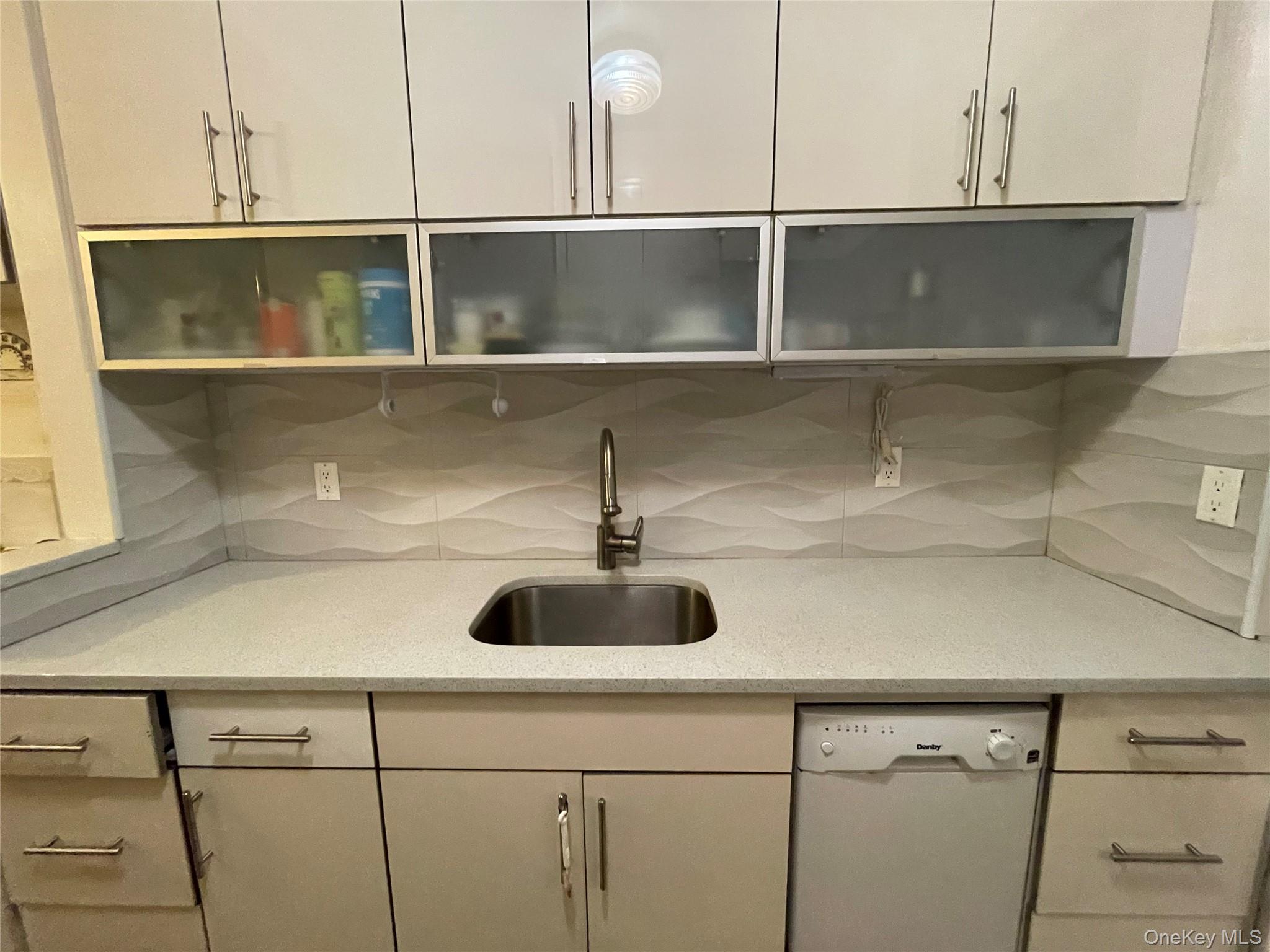 63-60 102nd Street, Unit D7 Queens, NY 11374 - Photo 40 of 41 Kitchen featuring light stone counters, white dishwasher, glass insert cabinets, and decorative backsplash