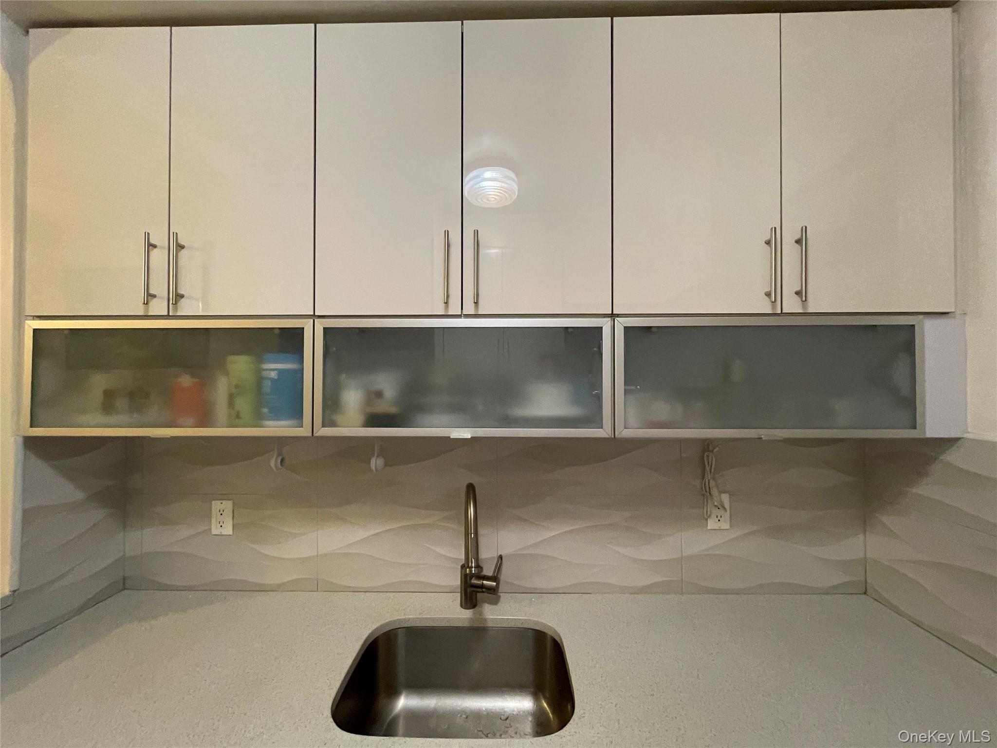 63-60 102nd Street, Unit D7 Queens, NY 11374 - Photo 41 of 41 Kitchen view of decorative backsplash, glass insert cabinets, and light stone counters