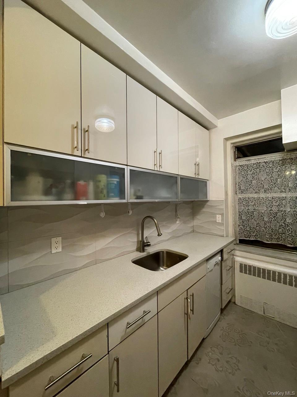 63-60 102nd Street, Unit D7 Queens, NY 11374 - Photo 10 of 41 Kitchen with tasteful backsplash, light stone countertops, radiator heating unit, white cabinetry, and white dishwasher