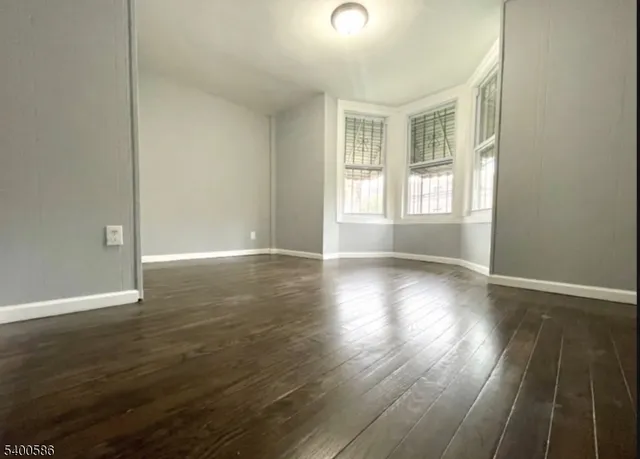 an empty room with wooden floor and windows with curtains