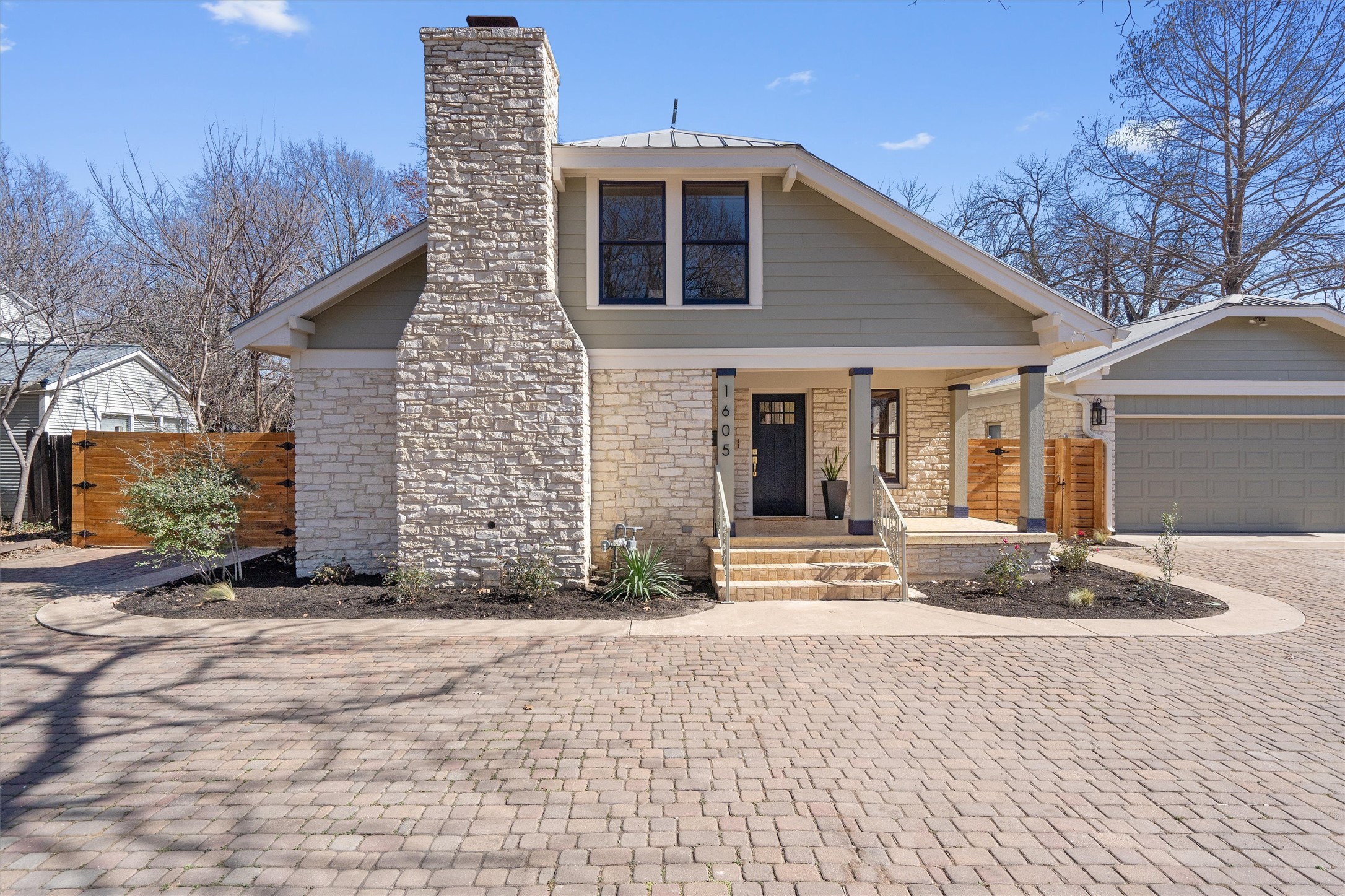 View of front of home featuring covered porch, a chimney, decorative driveway, a garage, and stone siding