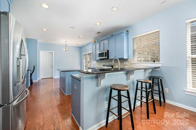 a kitchen with stainless steel appliances granite countertop white cabinets a refrigerator a stove a sink and a stove with wooden floor