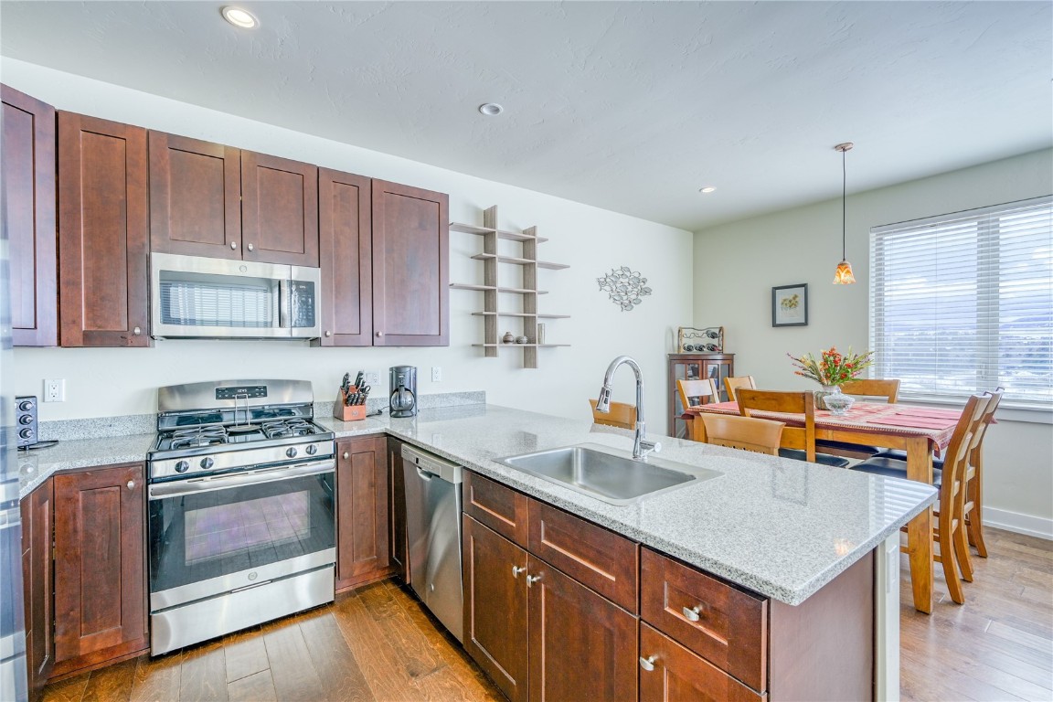Kitchen with a peninsula, light wood finished floors, appliances with stainless steel finishes, a sink, and light stone counters