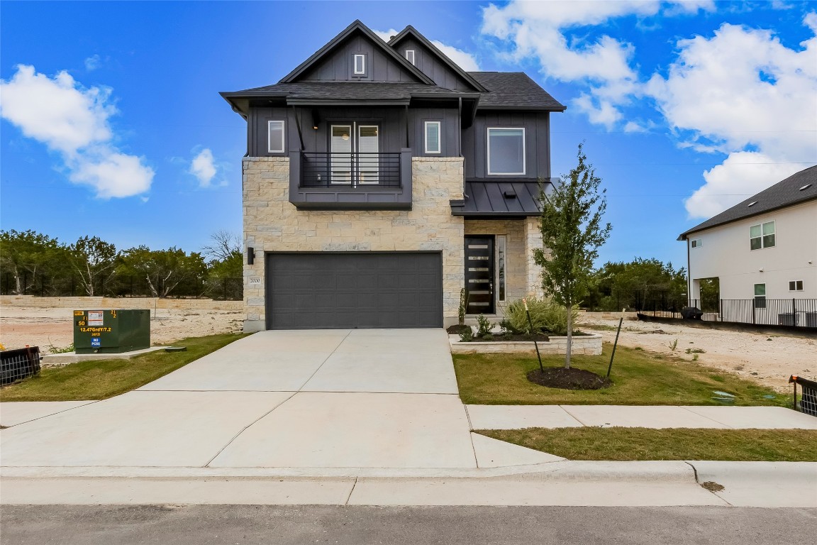 View of front facade with a balcony, stone siding, a garage, and driveway
