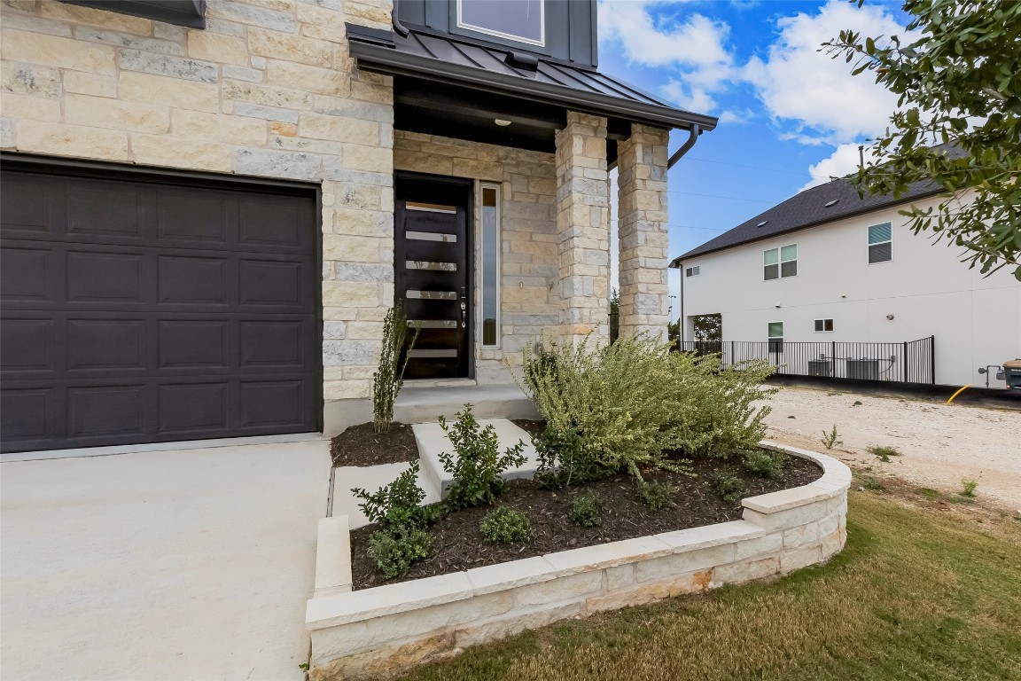 2000 Kit Circle Austin, TX 78758 - Photo 2 of 34 Entrance to property featuring a standing seam roof, stone siding, a metal roof, and a garage