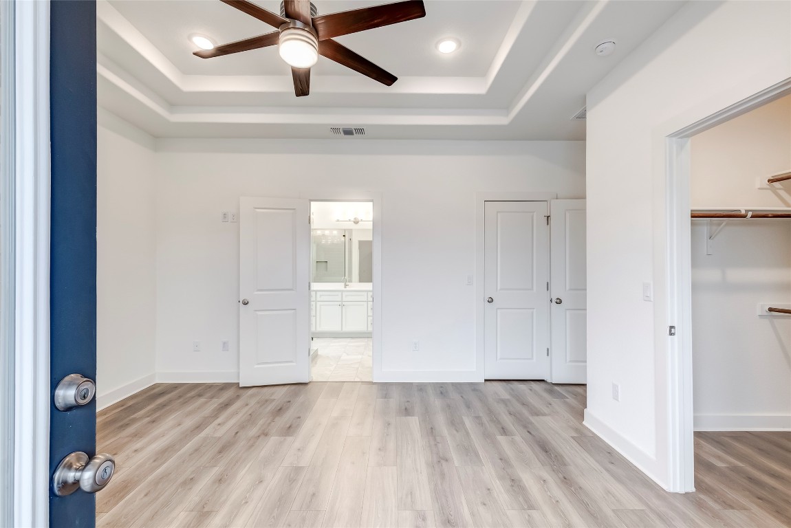 2000 Kit Circle Austin, TX 78758 - Photo 20 of 34 Unfurnished bedroom with recessed lighting, light wood finished floors, a ceiling fan, a tray ceiling, and a walk in closet