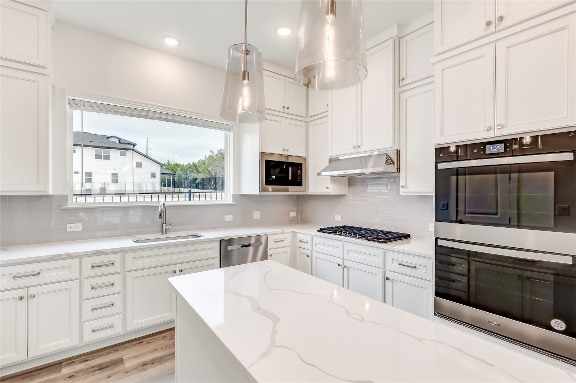 2000 Kit Circle Austin, TX 78758 - Photo 10 of 34 Kitchen featuring stainless steel appliances, white cabinets, light wood finished floors, light stone counters, and pendant lighting