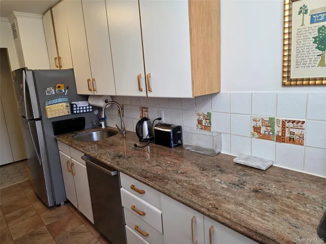 a kitchen with stainless steel appliances granite countertop a sink a stove and a refrigerator with white cabinets