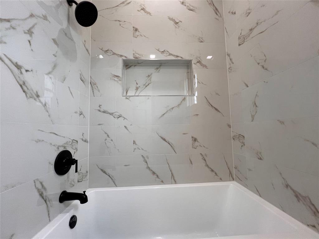121 Cartwright Park Road Weatherford, TX 76087 - Photo 12 of 17 Bathtub with matte black fixtures, white tile surround with gray veining, and a recessed shower niche