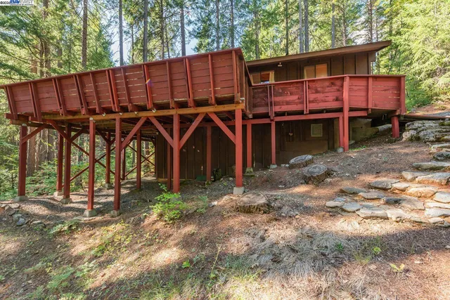 a view of a wooden house with large trees and wooden fence