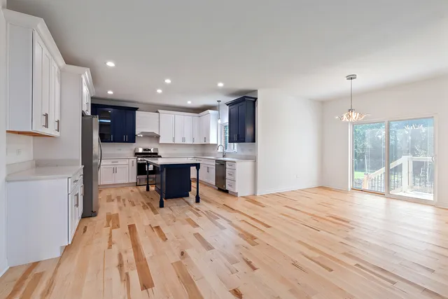 a kitchen with stainless steel appliances kitchen island granite countertop a refrigerator oven a sink a dining table and chairs with wooden floor