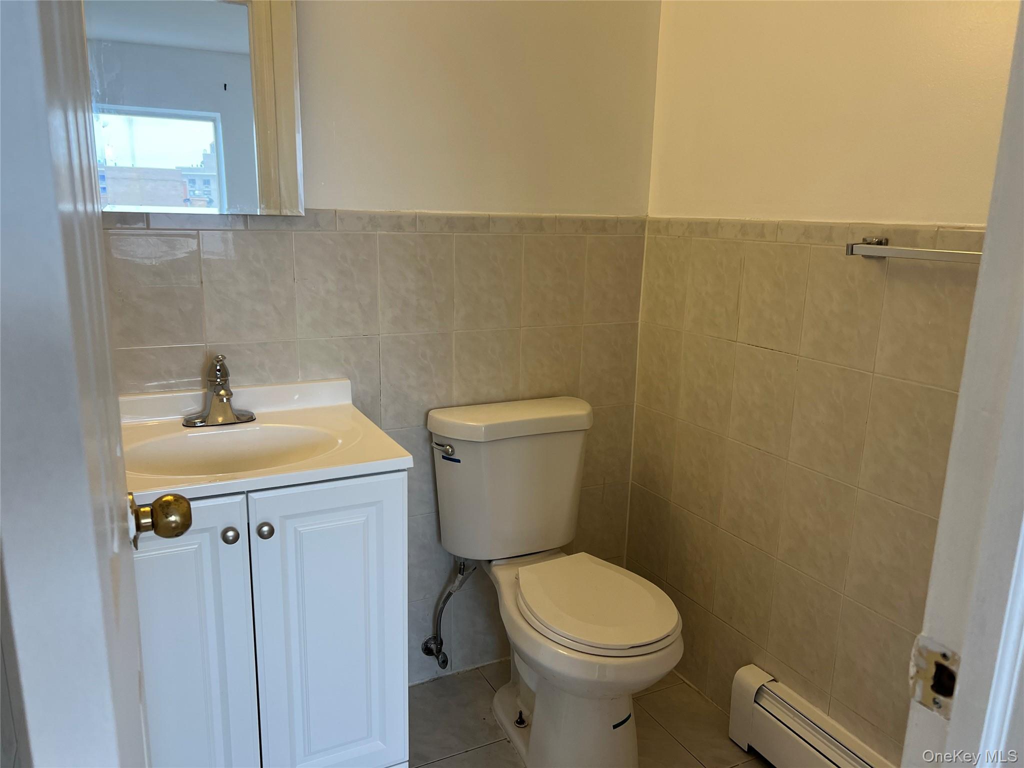 55-05 98th Street Queens, NY 11368 - Photo 11 of 12 Half bathroom featuring a baseboard heating unit, toilet, vanity, tile walls, and tile patterned flooring