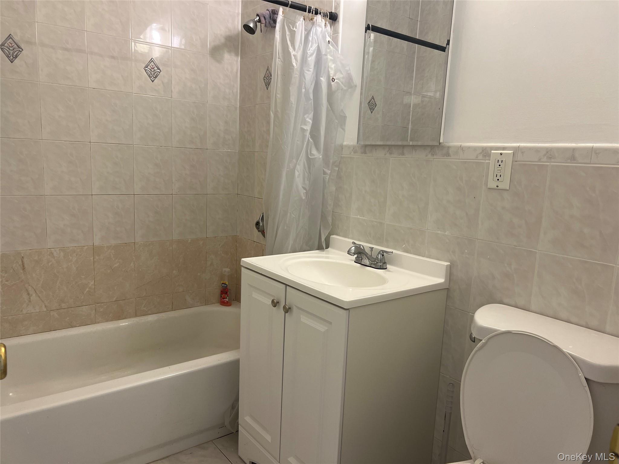55-05 98th Street Queens, NY 11368 - Photo 12 of 12 Bathroom with toilet, vanity, shower / bath combo with shower curtain, and tile walls
