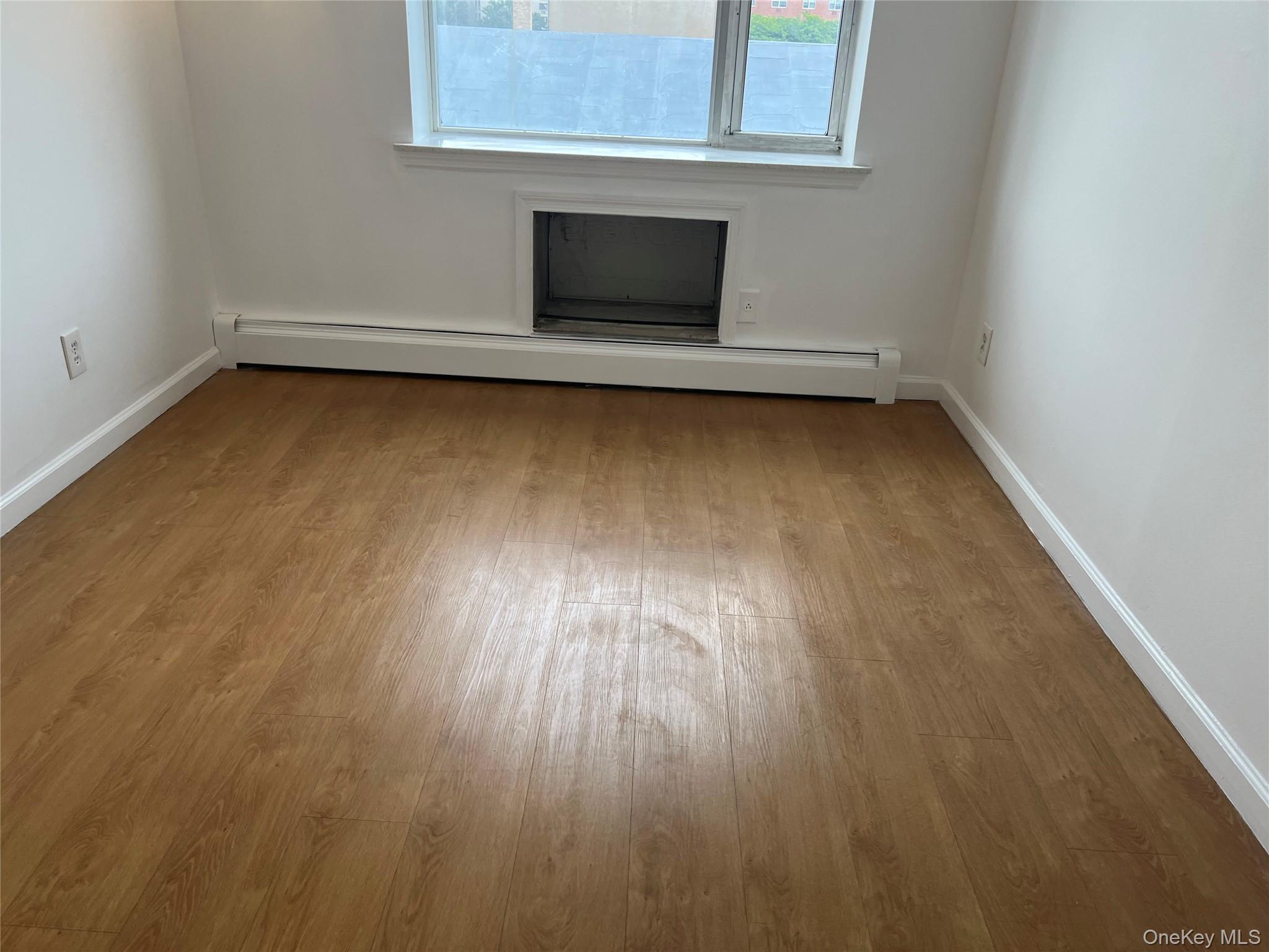 55-05 98th Street Queens, NY 11368 - Photo 4 of 12 Spare room featuring a baseboard radiator, wood finished floors, and baseboards